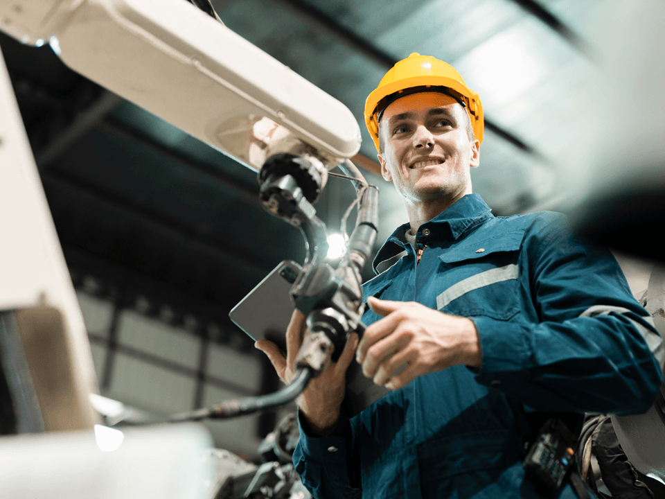 Man working in a factory holding an ipad in front of a machine