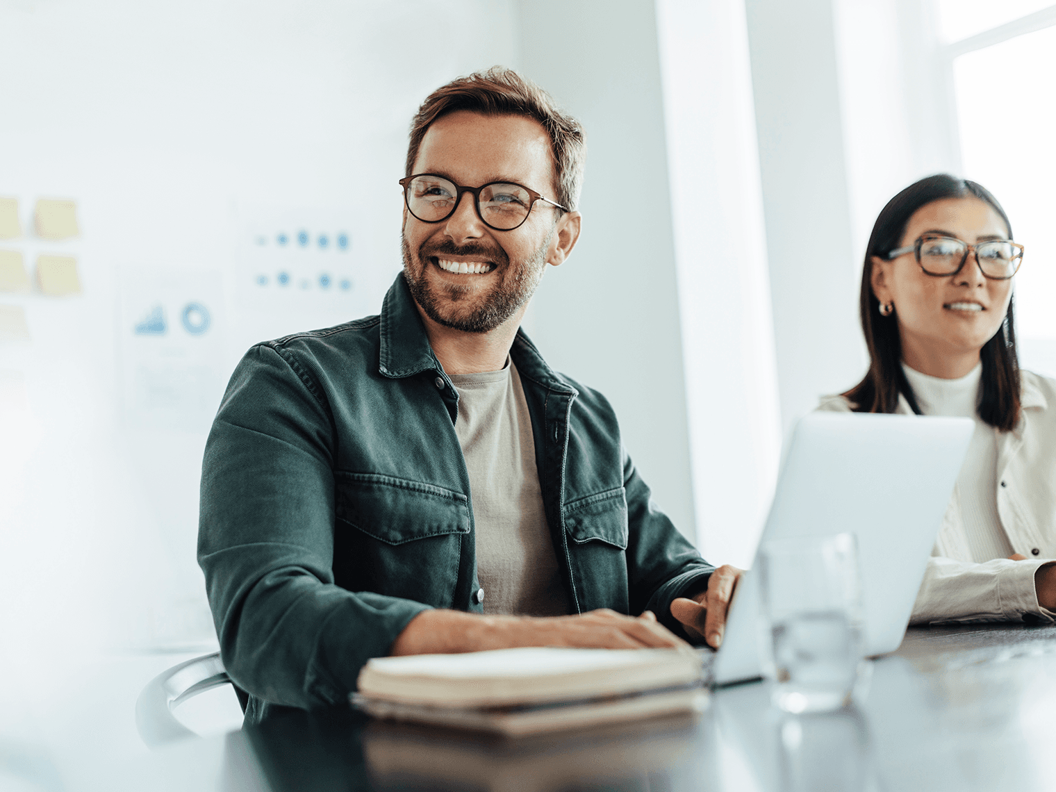 Man and woman with glasses sitting in a meeting smiling