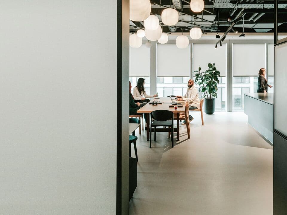 Office area with two women sitting down, one man sitting down, and one woman walking by