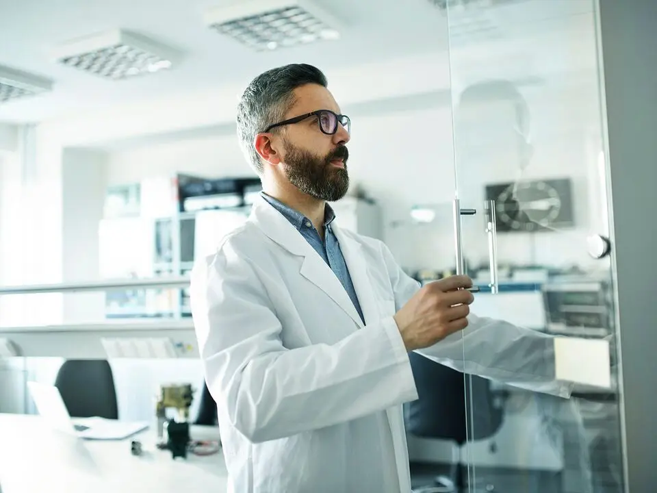 Man in lab coat with glasses opening a glass door