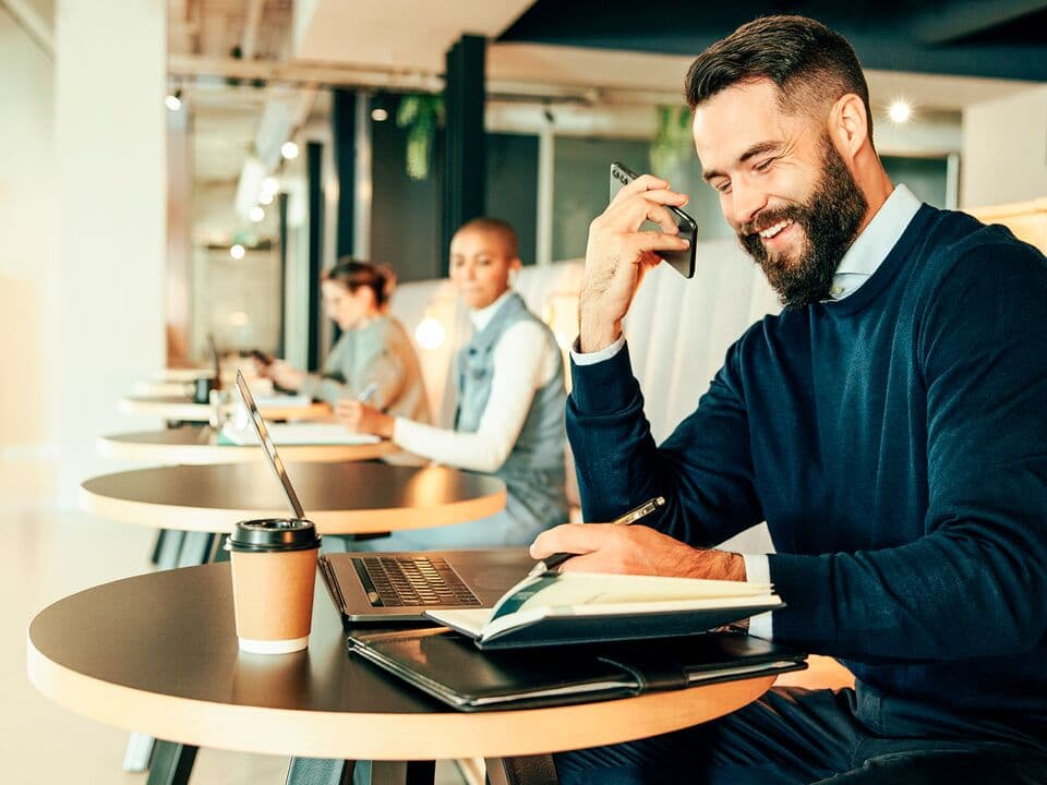 Man on a phone call in front of his computer sitting in a public space