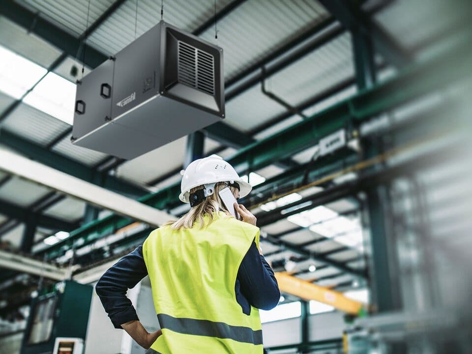 Woman with a phone inside a factory wearing a hardhat with a CamCleaner CC X-series