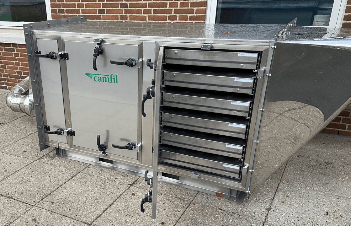 A stainless steel air filtration unit with multiple drawers, labeled and a logo positioned against a brick wall.